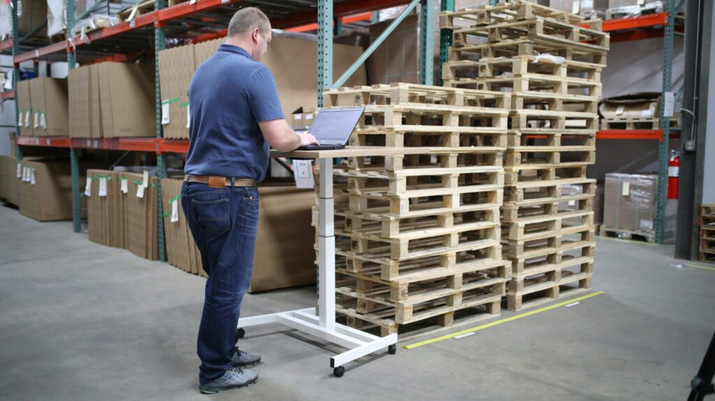 This is a picture of a manufacturer working from their laptop inside a warehouse to demonstrate 'Why More UK Manufacturers Are Ditching DIY Packing in 2025 (And What They’re Gaining Instead)'